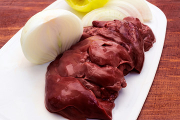 Chicken fresh liver, laid in pieces on a cutting Board with onions and green pepper.