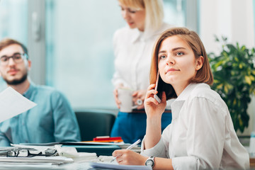 Young woman at the office talking on phone with team in background