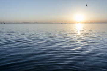 colorful sunset over water surface, evening sun over the bay, summer sky without clouds