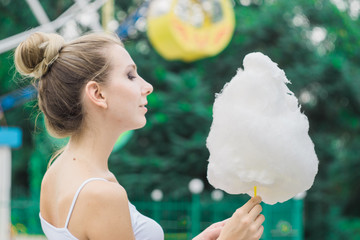 Cute model with cotton candy having fun in the park. Happy girl eating sweet treat bringing back childhood memories. Woman posing and smiling