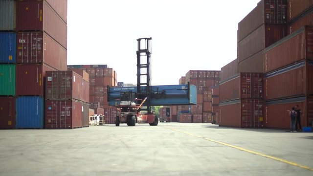 Shipping container loader truck transporting box. Shipyard piled high with containers being moved by machinery. Industrial loading yard with loading vehicle.