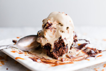 Melting ice cream on slice of chocolate cake with plate and spoon