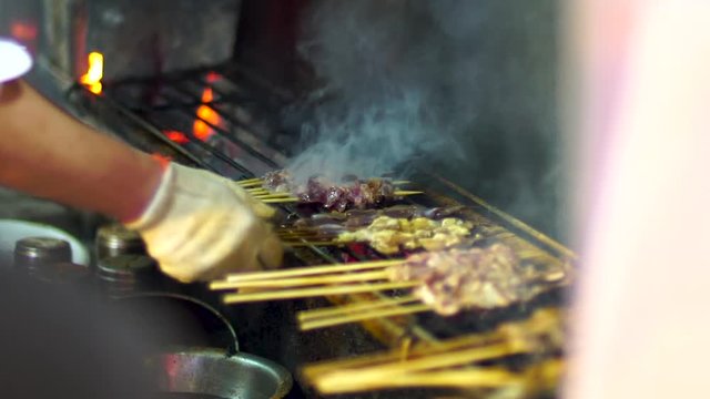 Slow motion cooking barbecue skewers in Chinese restaurant. Man uses hands to BBQ meat and vegetable sish kebab on coal fired grill. Traditional street food cooked by hand.