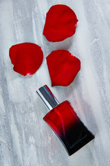 red perfume bottle, red rose petals on a gray background