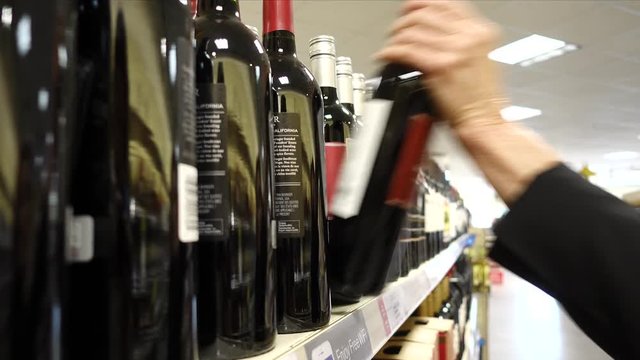 Selecting wine bottle from shelf. A hand takes a bottle of wine from the shelf. Shopping, and choosing a bottle of wine from the large selection to buy, grabbing it from the display rack.
