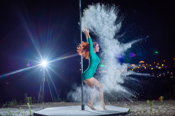 Red-haired woman in green body dancing on the pole and throwing flour against the city's city...