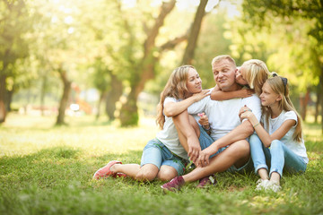 Naklejka na ściany i meble Cheerful family sitting on the grass during a picnic in the park