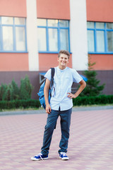 cute, young boy in blue shirt stands  in front of school with blue backpack and thumb up. Education, back to school concept