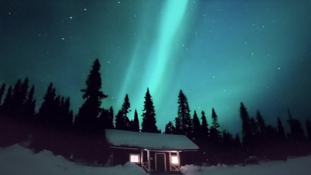 Aurora borealis STEVE phenomenon lights up the night sky above a cozy wilderness cabin in a winter pine forest, timelapse.