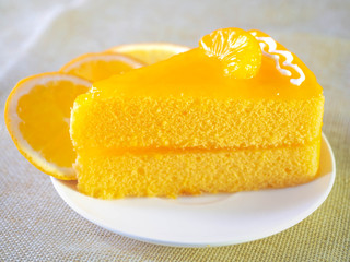 Orange cake on white dish and wooden fork is on table.