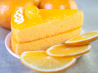 Naklejka na ściany i meble Orange cake on white dish and wooden fork is on table.