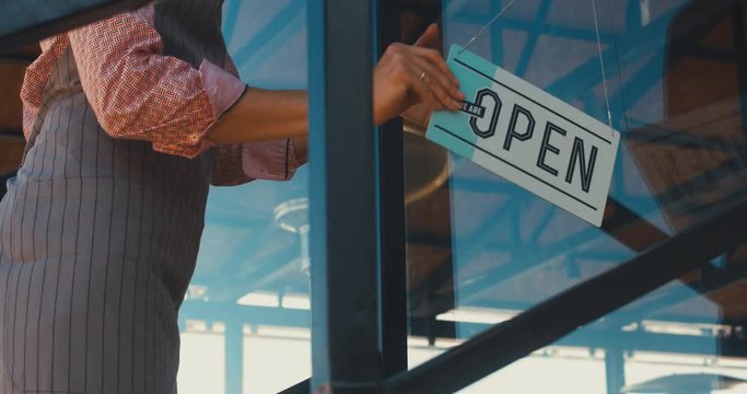 CU Caucasian female turning sign from closed to open on the entrance door of her small cafe. Small business concept. 4K UHD 60 FPS SLOW MOTION