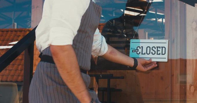 Caucasian male turning sign from open to closed on the entrance door of his small cafe. Out of business. 4K UHD 60 FPS SLOW MOTION