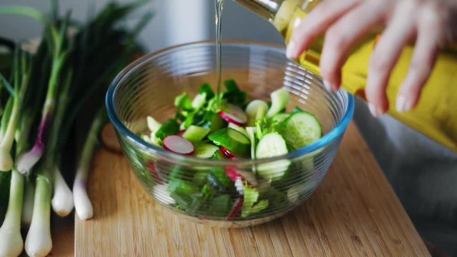 Woman hands pouring olive oil into glass bowl with fresh spring salad. Close up cooking woman hands. Natural vegetarian salad with onion, cucumber and radishes. Healthy lifestyle with organic food