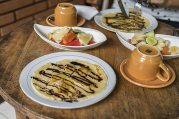 breakfast table setting with banana omelet and fresh mixed fruit salad, with coffee or tea cups in bali homestay