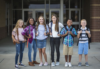 Large Group portrait of pre-adolescent school kids smiling in front of the school building. Back to school photo of a diverse group of children wearing backpacks and ready to go to school - Powered by Adobe