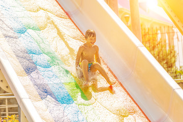 A happy boy on water slide in a swimming pool having fun during summer vacation in a beautiful aqua...