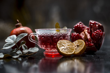 Close up of herbal and organic tea of pomegranate on wooden surface in transparent cup with raw pomegranate and sliced lemons with sugar.