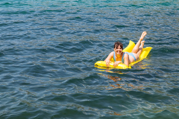 young adult woman on yellow mattress in blue sea water.