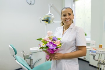 Female dentist smiling, with a bouquet of flowers, in dental office. National dentist's day.