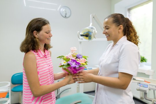 Girl patient gives a bouquet of flowers to a female doctor in dental office. National dentist's day.