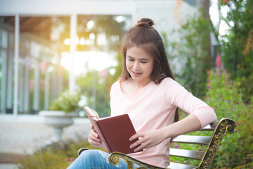 Fototapeta premium Beautiful asian girl sitting on bench reading book in park