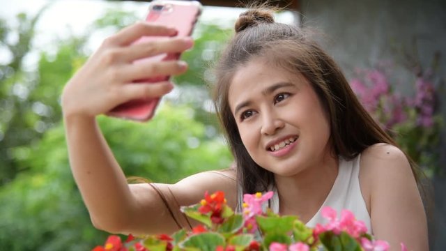 Beautiful asian girl taking her photo with flower by smartphone