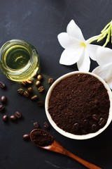 coffee ground scrub with beans, oil and plumeria flowers on black board background, beauty spa concept 