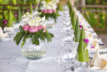 Pink flowers bouquet with green leafs decoration on the circle glass vase on the dinner table