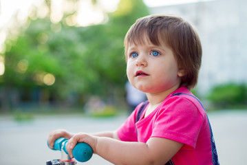 Little funny girl rides a bicycle. Baby on the scooter. Children's activity outside
