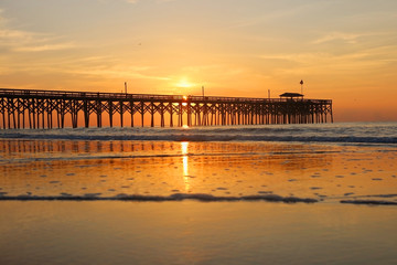 Cloudy sunrise over Atlantic ocean. Beautiful marine landscape with sun rising over calm atlantic ocean beach with wooden pier. South Carolina, Myrtle Beach area, USA. Vacation background.