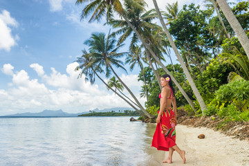 Tahiti luxury travel beach vacation woman walking in polynesian cover-up skirt beachwear on idyllic paradise island in French Polynesia. Red traditional clothes, bikini and flower girl.
