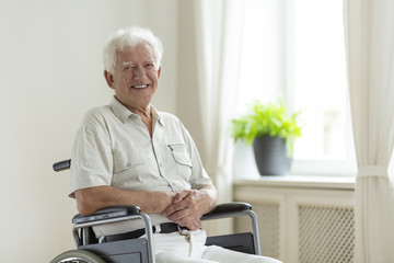 Smiling disabled senior man in the wheelchair alone at home