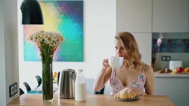 Happy girl having breakfast at home. Beautiful caucasian woman sitting at table and drinking coffee. Traditional breakfast with tea and fresh croissants. Morning time concept. Woman morning coffee