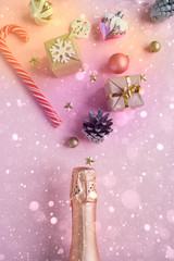 Champagne bottle with different christmas decoration on pink background. New year concept.