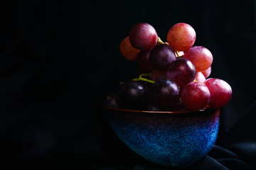 Red grapes in the dark, red grapes in a white bowl in the dark corner