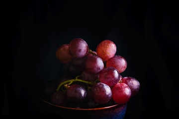 Red grapes in the dark, red grapes in a white bowl in the dark corner