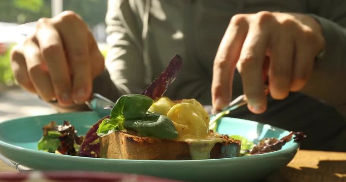 Crop close-up portrait of a man eats Benedict eggs and toasts with salad on street cafe