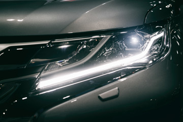 Car headlight and hood of powerful sports blue car with blue glare on dark background. Close up at...