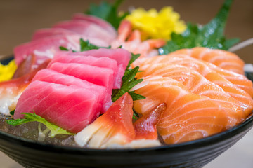 Mixed sliced fish sashimi on ice in black bowl. Sashimi Salmon Tuna Hamachi Prawn and Surf Calm set, raw fish, japanese food in Asian restuarant.