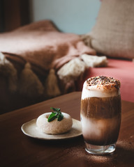 Chocolate Milk Shake with Coffee and Colorful Sugar Sprinkles As Topping and Blur doughnut and Mint Leaf on Wooden Table in Cafe