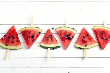 Watermelon slice popsicles on a white wooden background.