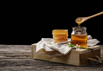 Honey bee in jar and honeycomb with honey dipper and flower on wooden table, bee products by...