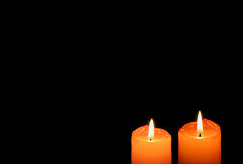 A pair of vivid orange color candles burning in the dark, with free space for text and design 