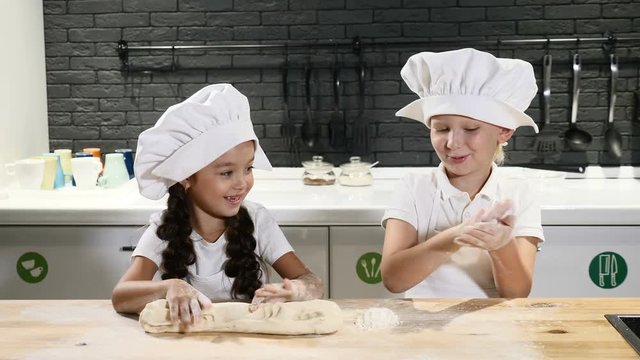 Pretending adults. Two kids in chef hats and aprons play with dought rolling and touching it. Cooking together concept. 4k