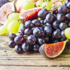 Fototapeta premium Still life of fresh autumn fruit. Grapes black and green, figs and leaves on a wooden table with copy space.
