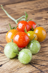 Cherry tomatoes in drops on a wooden table. A branch of multi-colored tomato green, yellow and red. Selective focus.