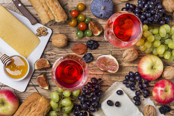 Cheese, wine, baguette grapes figs honey and snacks on the rustic wooden table top.
