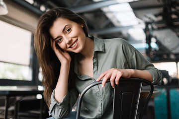 Fototapeta na wymiar Close up portrait of cheerful smiling woman sitting in loft modern coffee shop. Young beautiful and positive female posing for camera indoors. 