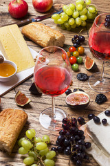 Cheese, wine, baguette grapes figs honey and snacks on the rustic wooden table top.